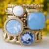 QUDO Interchangeable Stack of various gold bands displaying ring toppers in four shades of blue. The bottom two toppers and Fabero Flats.