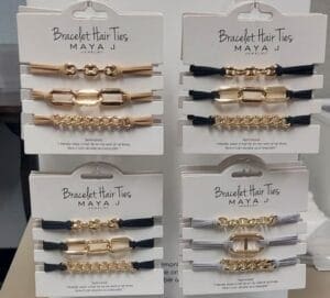 Maya J hair ties display featuring beige, black, and gray bracelets with gold details.