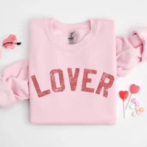 Light Pink Sweatshirt folded up on a white background with heart shaped lollipops. The sweatshirt features screen-printed red letters that say "Lover"